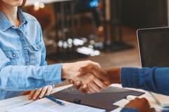 A white woman with red hair shakes hands across a desk with a Black man.