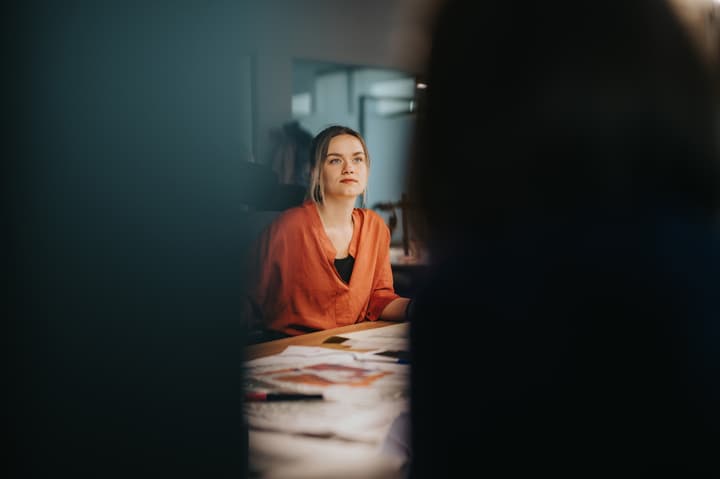 A focused businesswoman in an orange blouse engages in a meeting, discussing ideas and strategies in an office