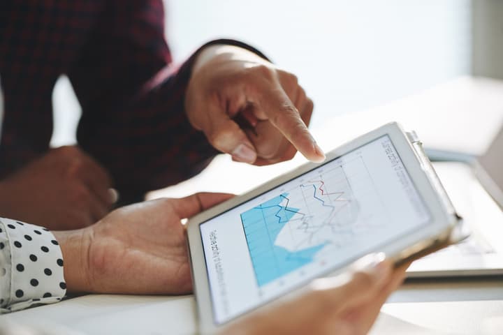 Close-up shot of crop man pointing at diagram on tablet screen while having discussion with colleague at workplace