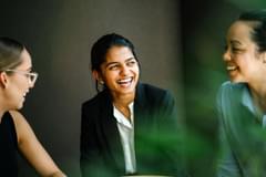A young Indian Asian woman is having a business meeting with her team in a conference room. Her colleagues are diverse with a Caucasian woman