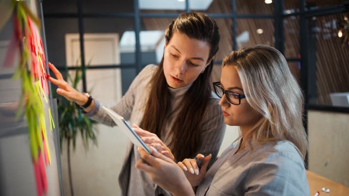 Two young businesswomen collaborate together on an Agile kanban board.