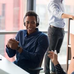 A Black, male call center worker smiles and laughs with his female coworker.