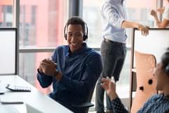 A Black, male call center worker smiles and laughs with his female coworker.