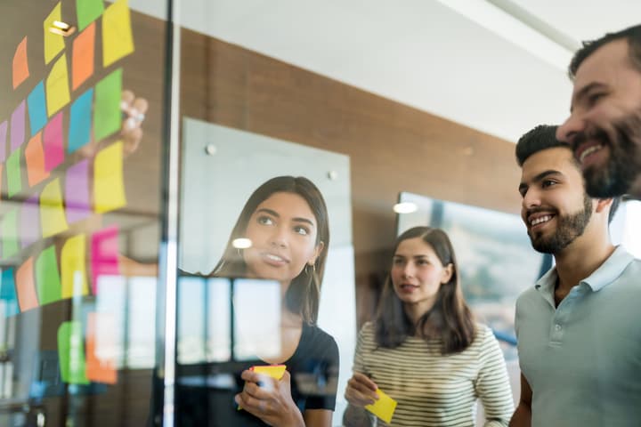 Two Women and Men Putting Sticky Notes on a Glass Wall Team Planning In Office