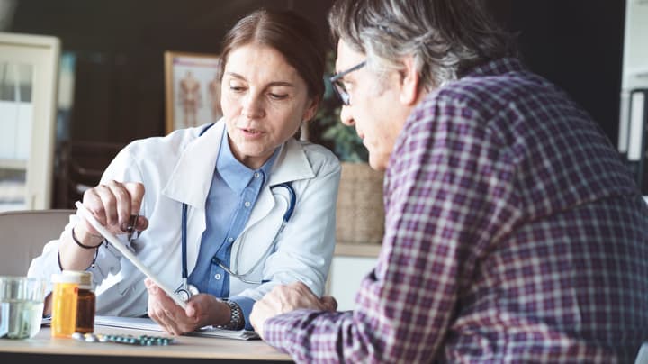 An older female doctor explains the contents on the screen of a digital tablet to an elderly, white male patient.