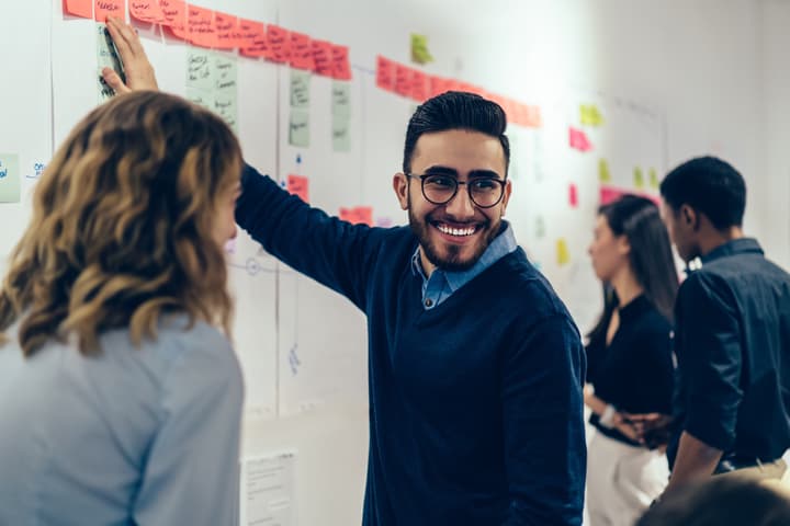Positive young man laughing while collaborating with colleagues on creating presentation using colorful sticky notes.