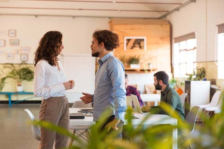 Focused male and female coworkers discussing project in meeting room. Business colleagues in casual standing together in contemporary office space.
