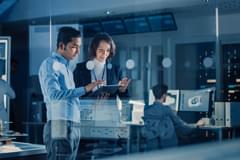 Two people examine data on a table in a room with servers