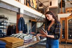 Female retail store worker with a tablet in front of clothes in a store