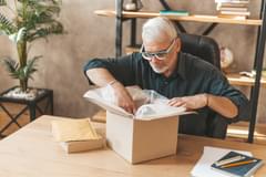 An older, white man opens a package for an online purchase.