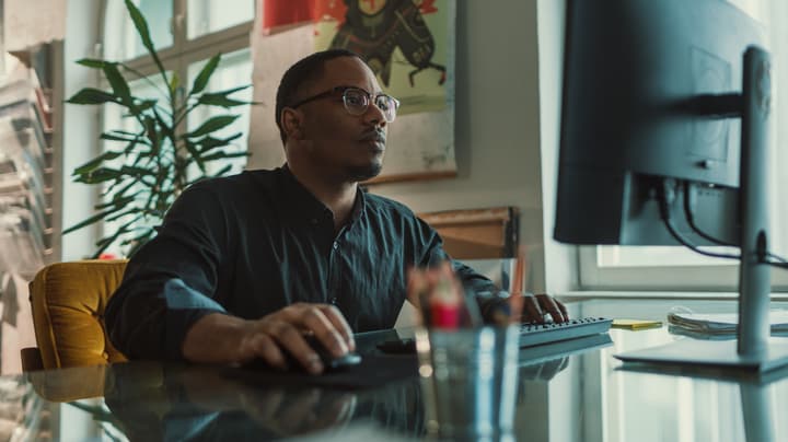 Man sits at computer at a desk working on a learning management system.