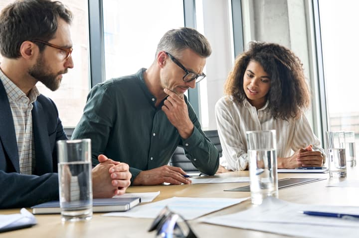 Two white men and one black woman sitting in conference room having discussion