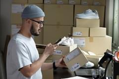 Asian male uses a mobile app on a smartphone to check the product information on a package he is preparing for shipment.