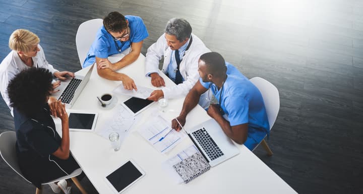 Team of medical workers sitting and meeting with laptops around table. Healthcare experts discussing papers and test results.