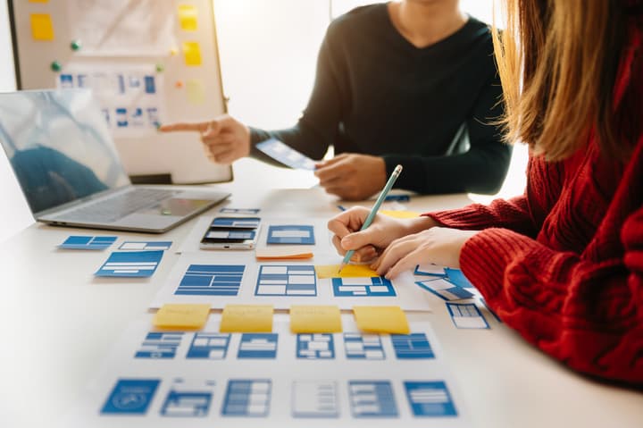 UX developer and ui designer brainstorming about mobile app interface wireframe design with customer brief and color code at modern office.