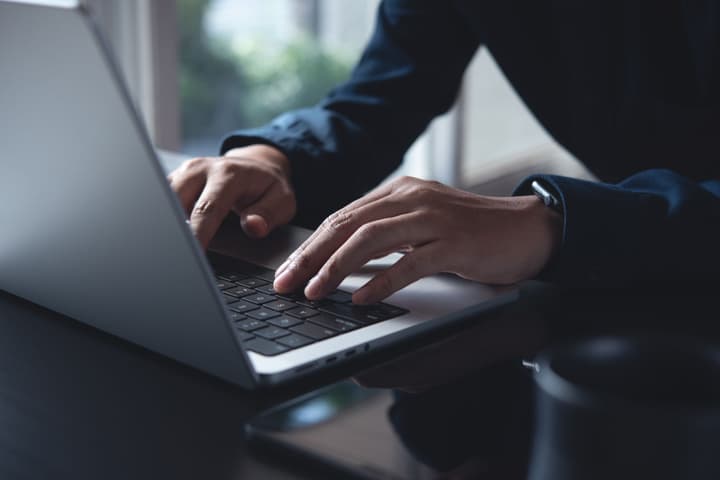 A close-up shot of a man's hands typing on a laptop