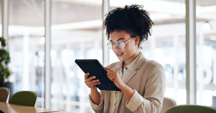 A black woman is standing while looking at a tablet and professionally dressed