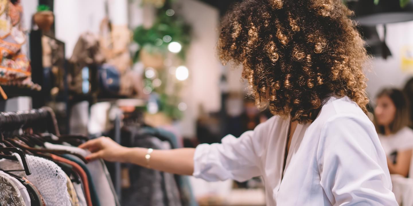 Customer experience trends for 2023 with a photo of a curly-haired woman in a store reaching forward and looking at clothes on a rack.