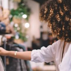 Customer experience trends for 2023 with a photo of a curly-haired woman in a store reaching forward and looking at clothes on a rack.