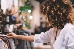 Customer experience trends for 2023 with a photo of a curly-haired woman in a store reaching forward and looking at clothes on a rack.