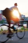 A bicyclist rides a bike along the Willamette River in Portland, OR at sunset. The Broadway Bridge is in the background.