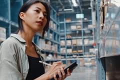A female in a warehouse looking at shelves while taking notes.