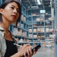 A female in a warehouse looking at shelves while taking notes.