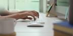 Close up of male entrepreneur's hands typing on computer keyboard on white office desk in modern office room