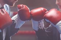 Close up of two business men in suits wearing boxing gloves in a boxing ring. Their gloves are touching.