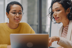 Two women of color collaborate around a laptop computer in a modern office space.