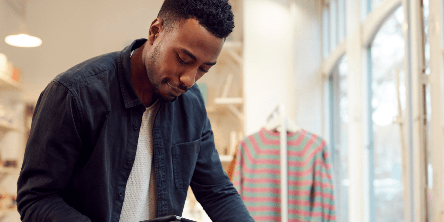 Black man in a dark blue long-sleeve shirt in a retail store holding a tablet while working.