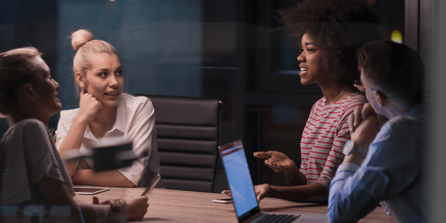 Five business people of various genders and races collaborate around a meeting table in a modern office.
