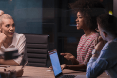 Five business people of various genders and races collaborate around a meeting table in a modern office.