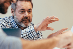 Three medical professionals gather around a digital tablet and discuss the items on the tablet's screen during a meeting.