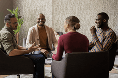 A group of four business people of various ages, races, and genders gather around a coffee table and engage in a lively conversation.