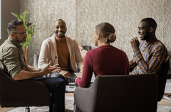 A group of four business people of various ages, races, and genders gather around a coffee table and engage in a lively conversation.