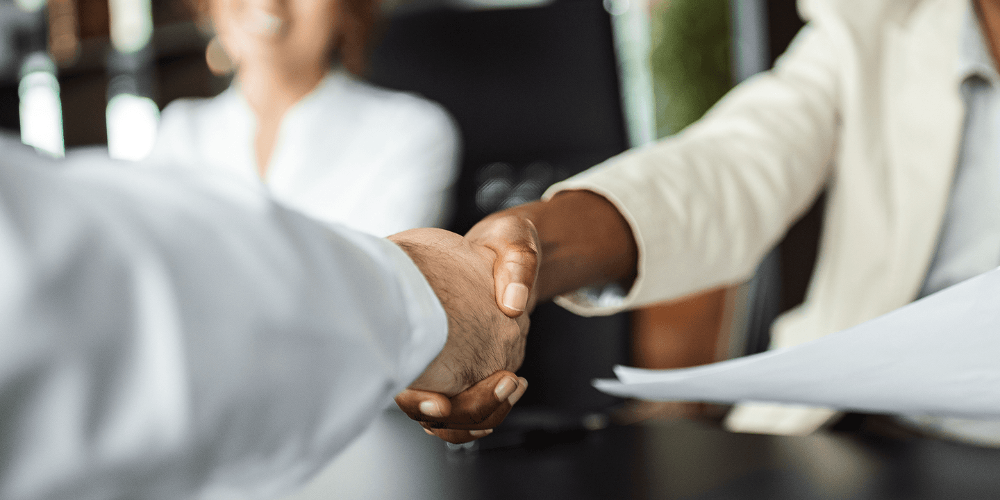Close up image of two business people shaking hands. One is a white man, the other is a Black woman.