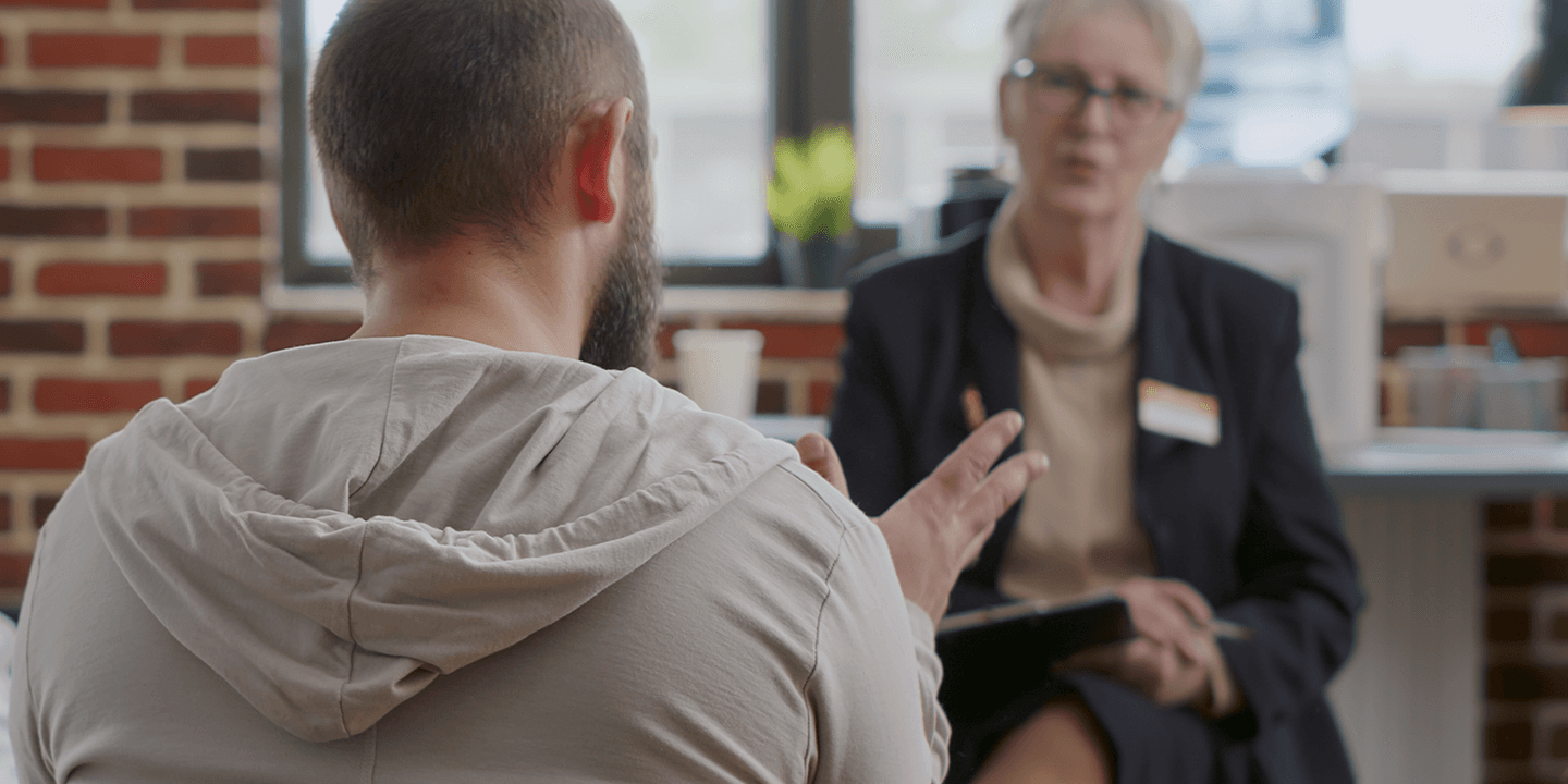 Two men, one a Black man, the other white, talk to a female moderator wearing a name tag during a tense group discussion.