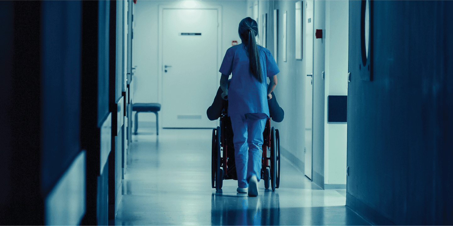 A healthcare worker batting burnout pushes a wheelchair in a hospital